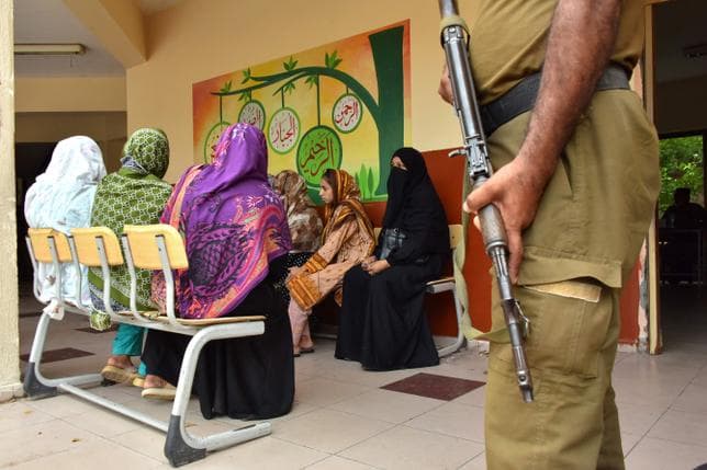 Un policier tient la garde devant un groupe de femmes qui s’apprêtent à aller voter à Muzaffarabad afin d’élire les députés au Parlement du Cachemire pakistanais.